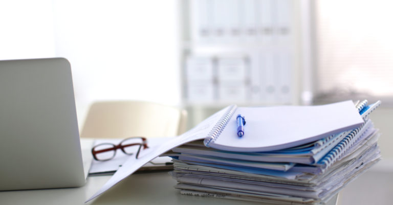 Contract drafting represented by stack of papers and computer on desk